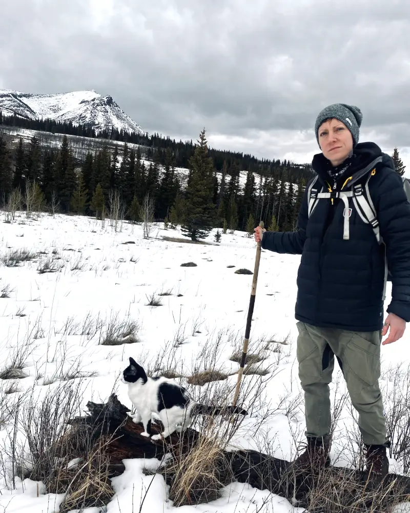 Jade Stevens, founder of REWILD Mushrooms, hiking in the snowy Rockies with her black and white cat